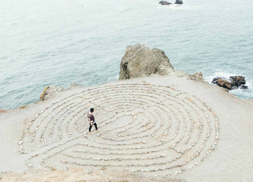 Zu sehen ist ein Stein-Labyrinth. Eine Frau geht durch das Labyrinth. Das Labyrinth ist vor einem Felsvorsprung mit angrenzendem Meer.<br />
Die psychotherapeutische Beratung hilft durch das eigene Labyrinth zu finden.